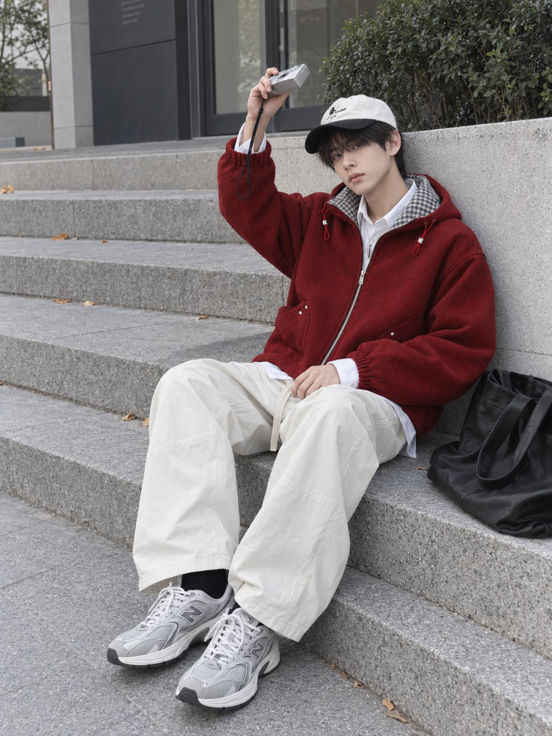 男生穿酒紅連帽外套和米白寬褲坐在石階上，搭配黑白棒球帽與灰銀球鞋